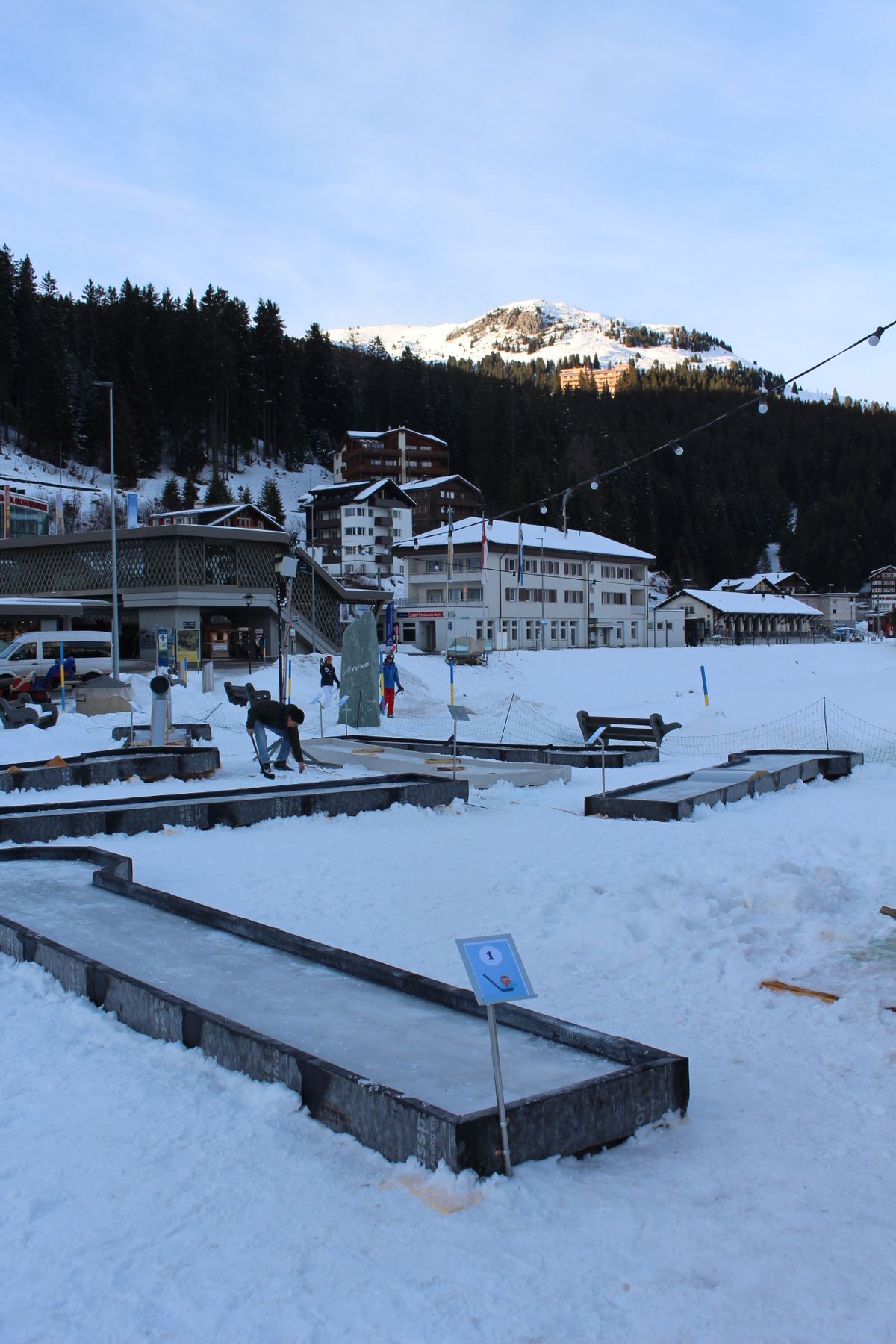 Die Eisminigolf-Anlage auf dem Postplatz bei Tag, im Hintergrund Bahnhof und Berge